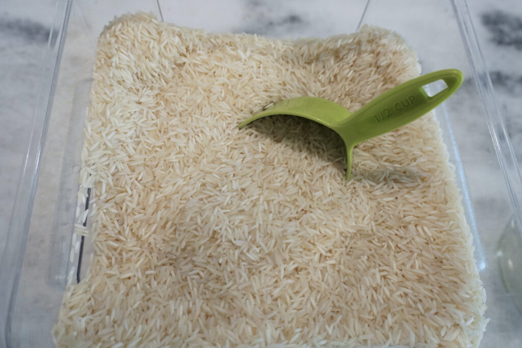 a bin of rice grains with a measuring cup in it
