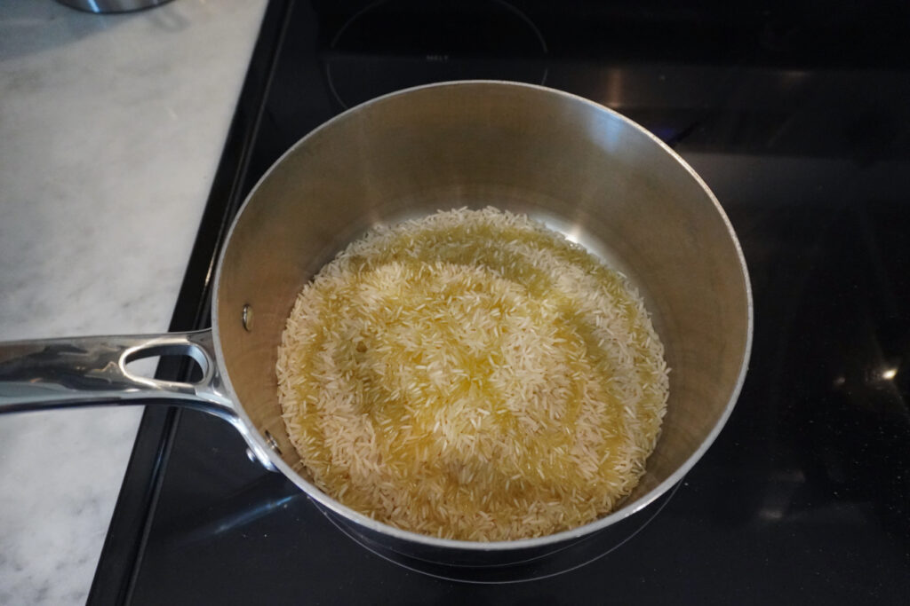 uncooked basmati rice with olive oil drizzled over it in a stainless steel pot
