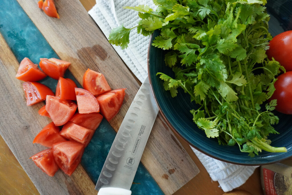 chopped tomatoes on a cutting board and a bunch of cilantro in a blue bowl
