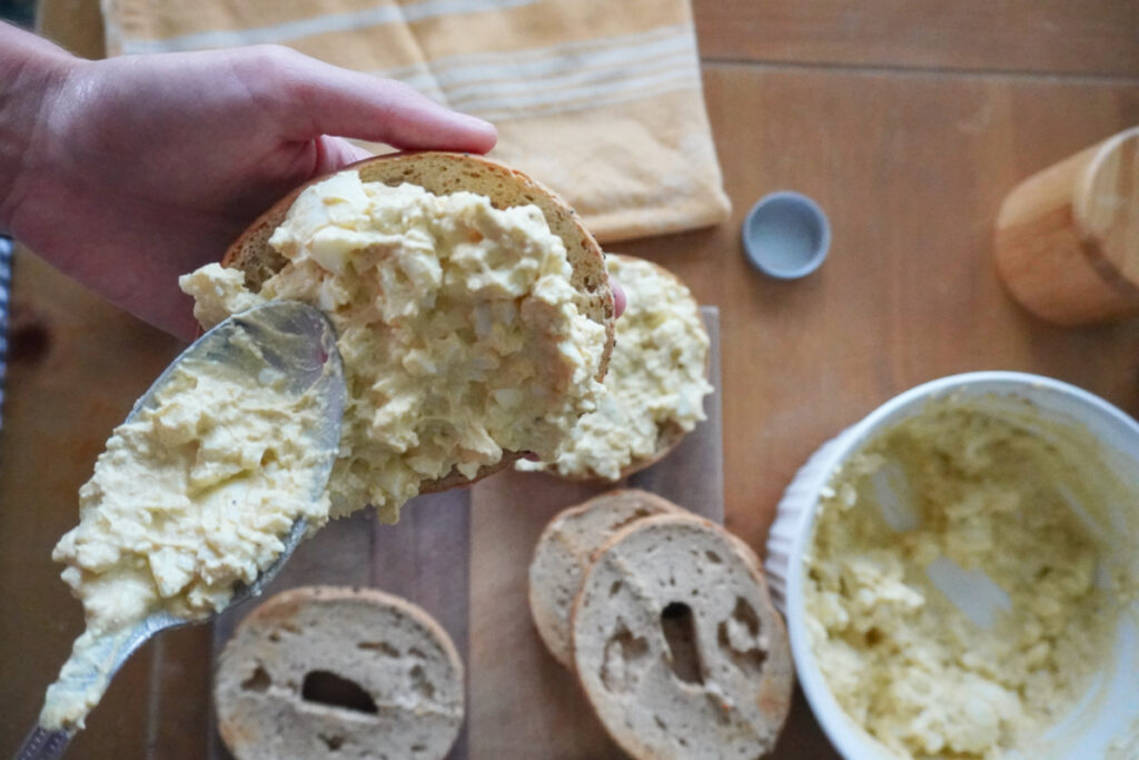 woman spreading egg salad onto a bagel
