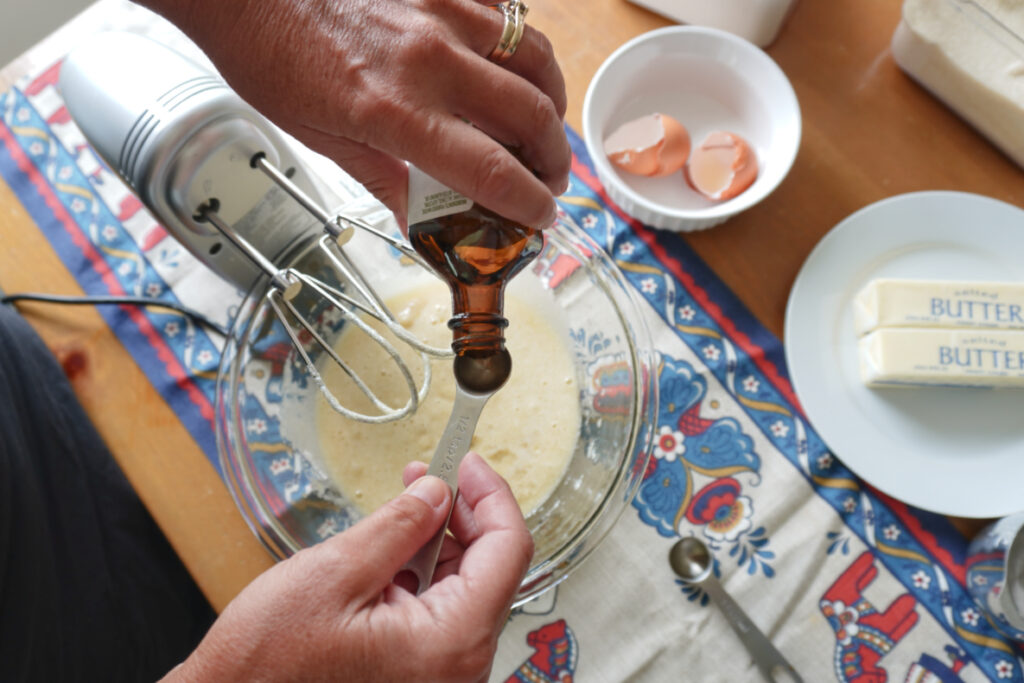 woman measuring out almond extract over a mixing bowl of almond skillet cake batter