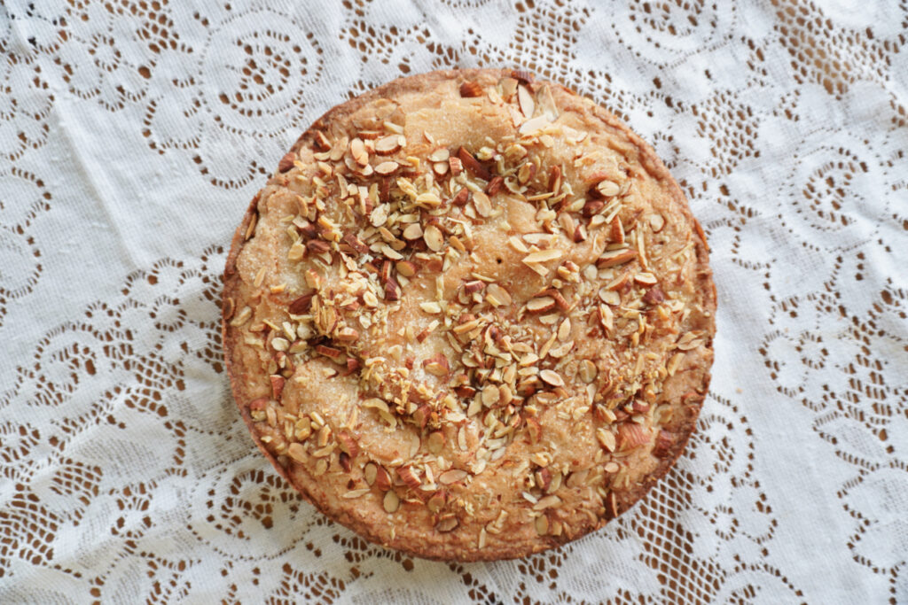A whole unsliced round almond skillet cake on a white lace tablecloth