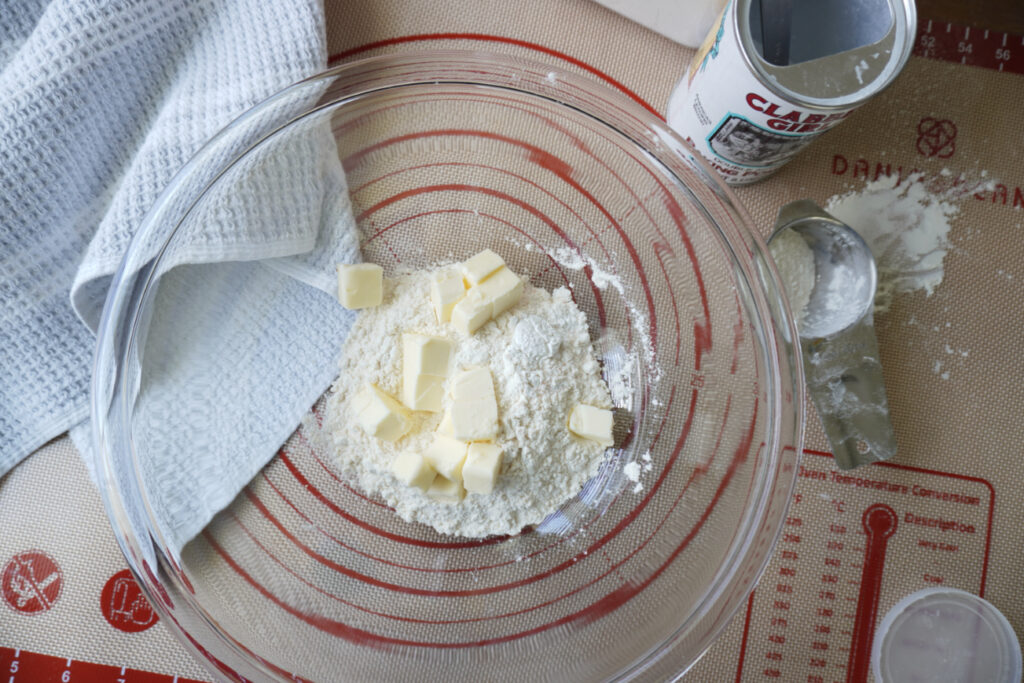 a glass mixing bowl of dough ingredients: flour, baking powder, salt, and cubed butter