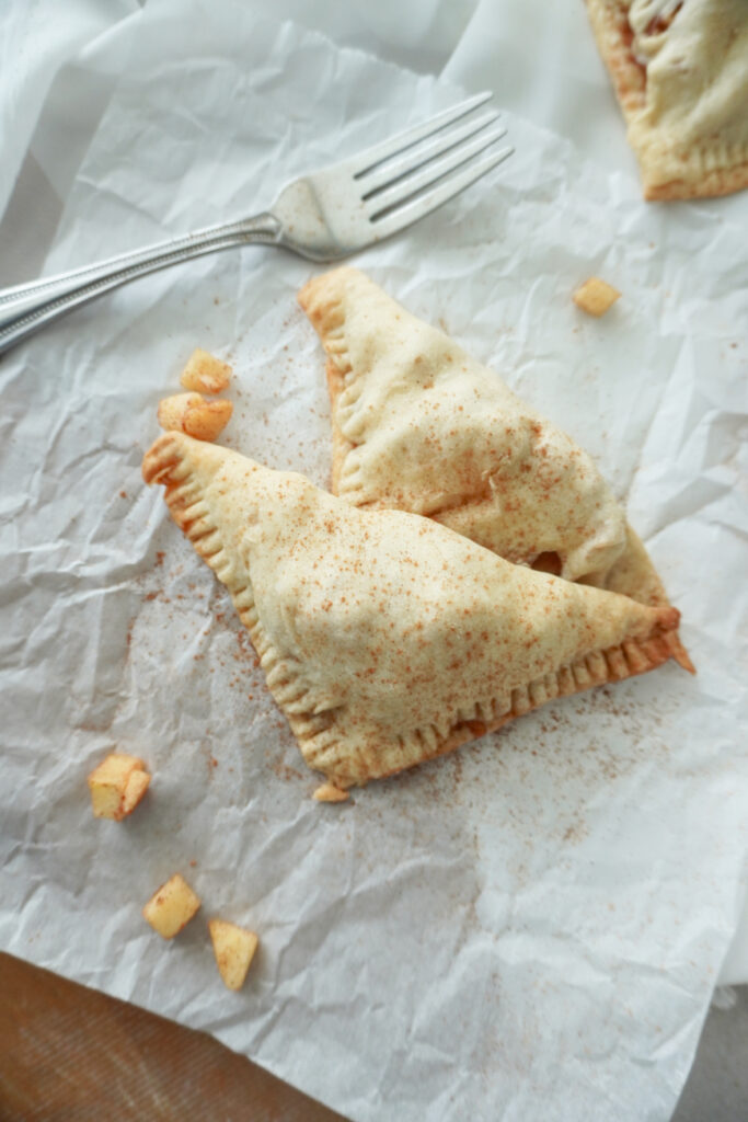 two apple turnovers sprinkled with cinnamon on white parchment paper with a fork