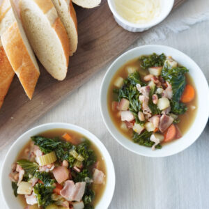 2 bowls of black eyed pea vegetable soup with a sliced baguette and butter