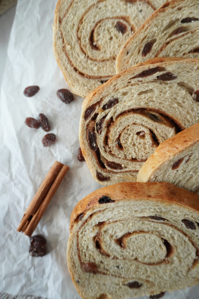 slices of cinnamon raisin bread lined up with cinnamon sticks and raisins beside them