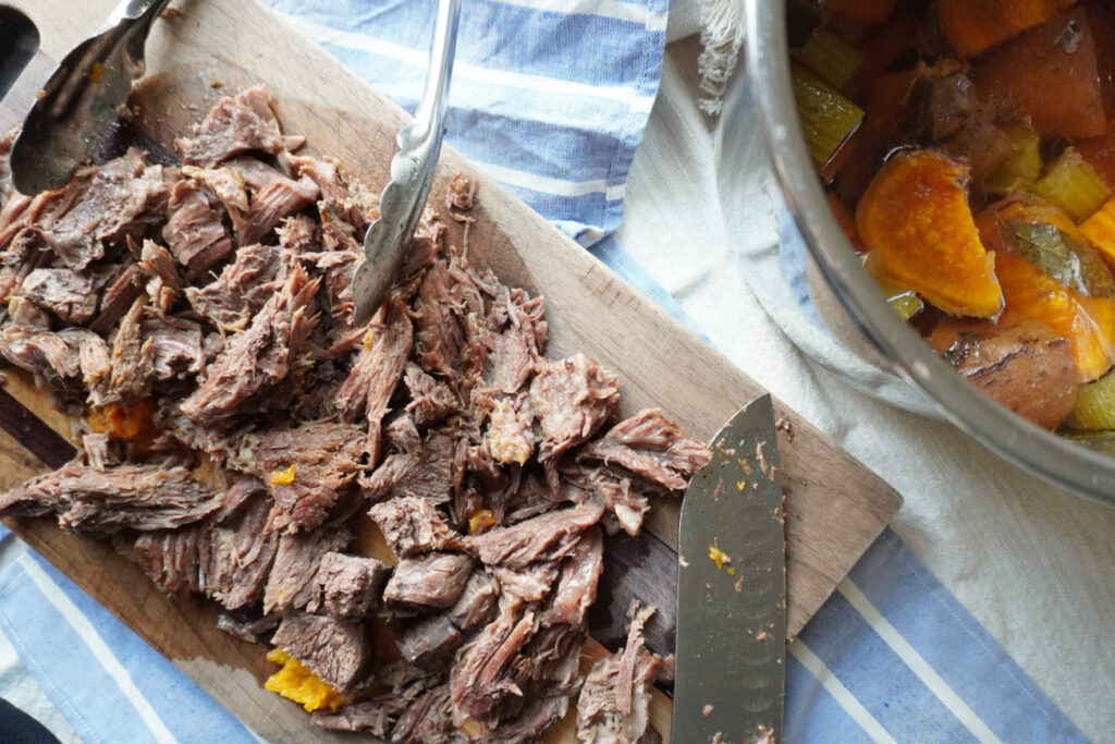 shredded pot roast on a cutting board next to an Instant Pot of veggies and broth