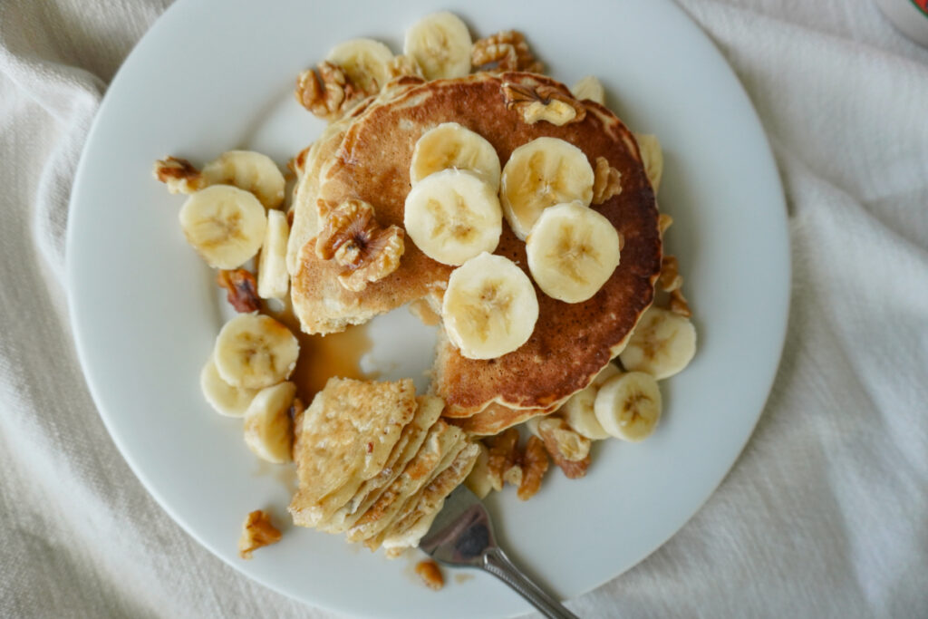 an overhead view of a stack of pancakes topped with bananas and walnuts