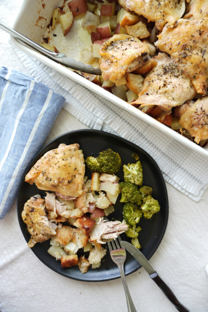 a black plate of chicken, sourdough bread stuffing, and roasted broccoli beside a baking dish of chicken and stuffing