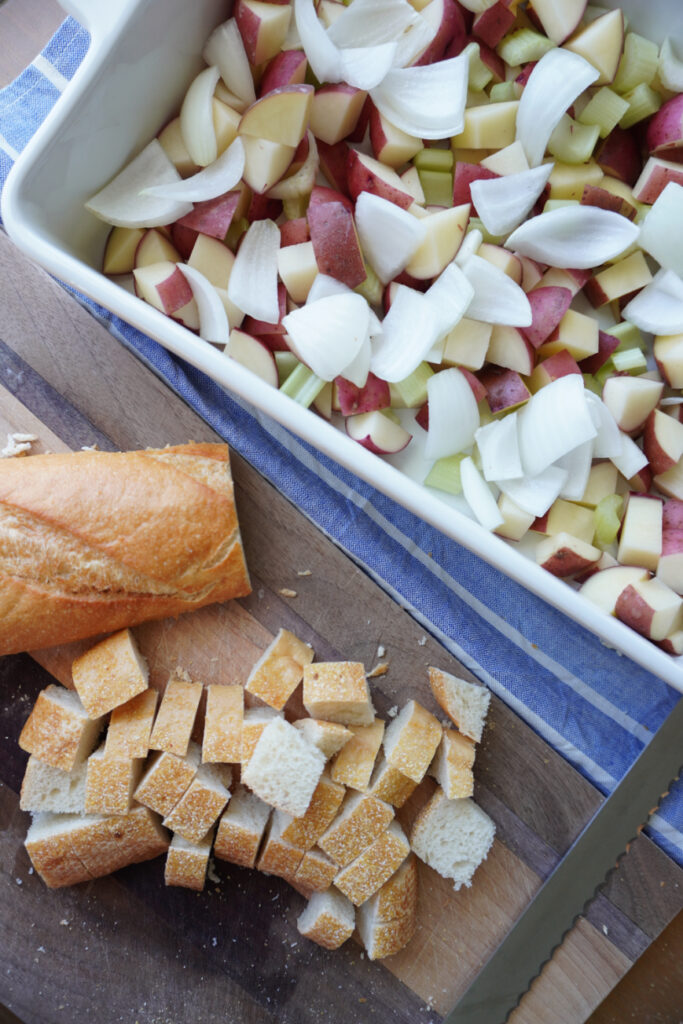 a cut up sourdough baguette beside a baking dish of potatoes, celery, and onions