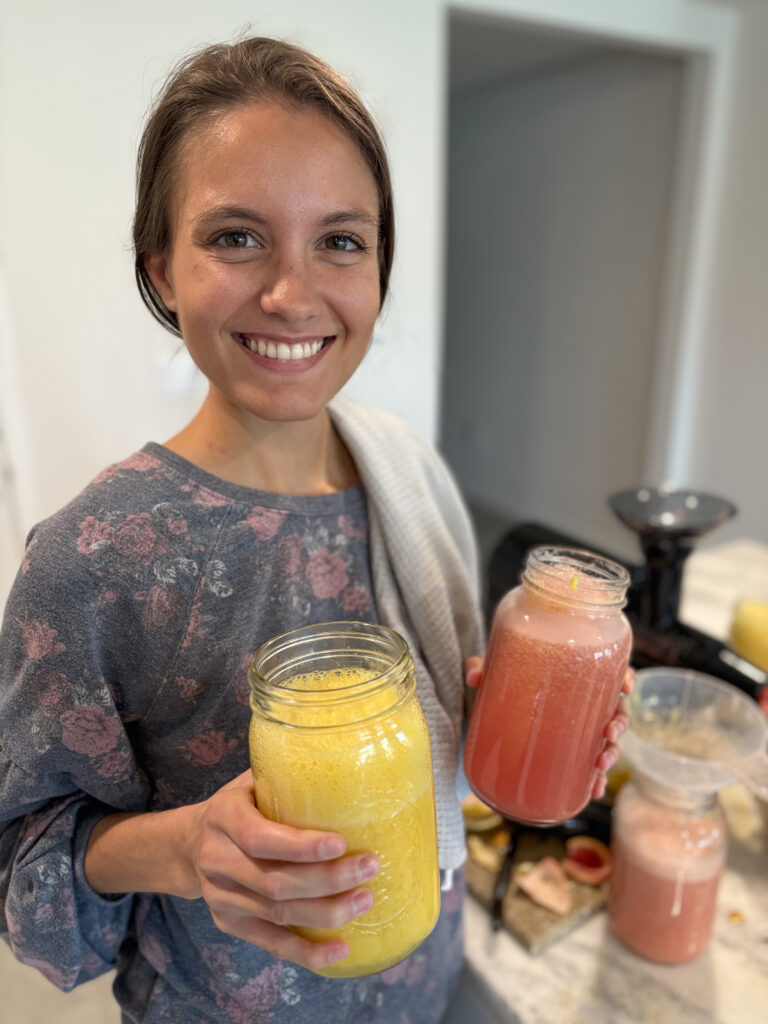 woman smiling while holding a jar of orange juice and a jar of grapefruit juice