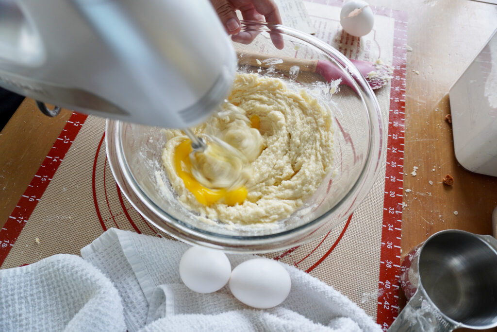 eggs being beaten into a bowl of batter with a handheld electric mixer