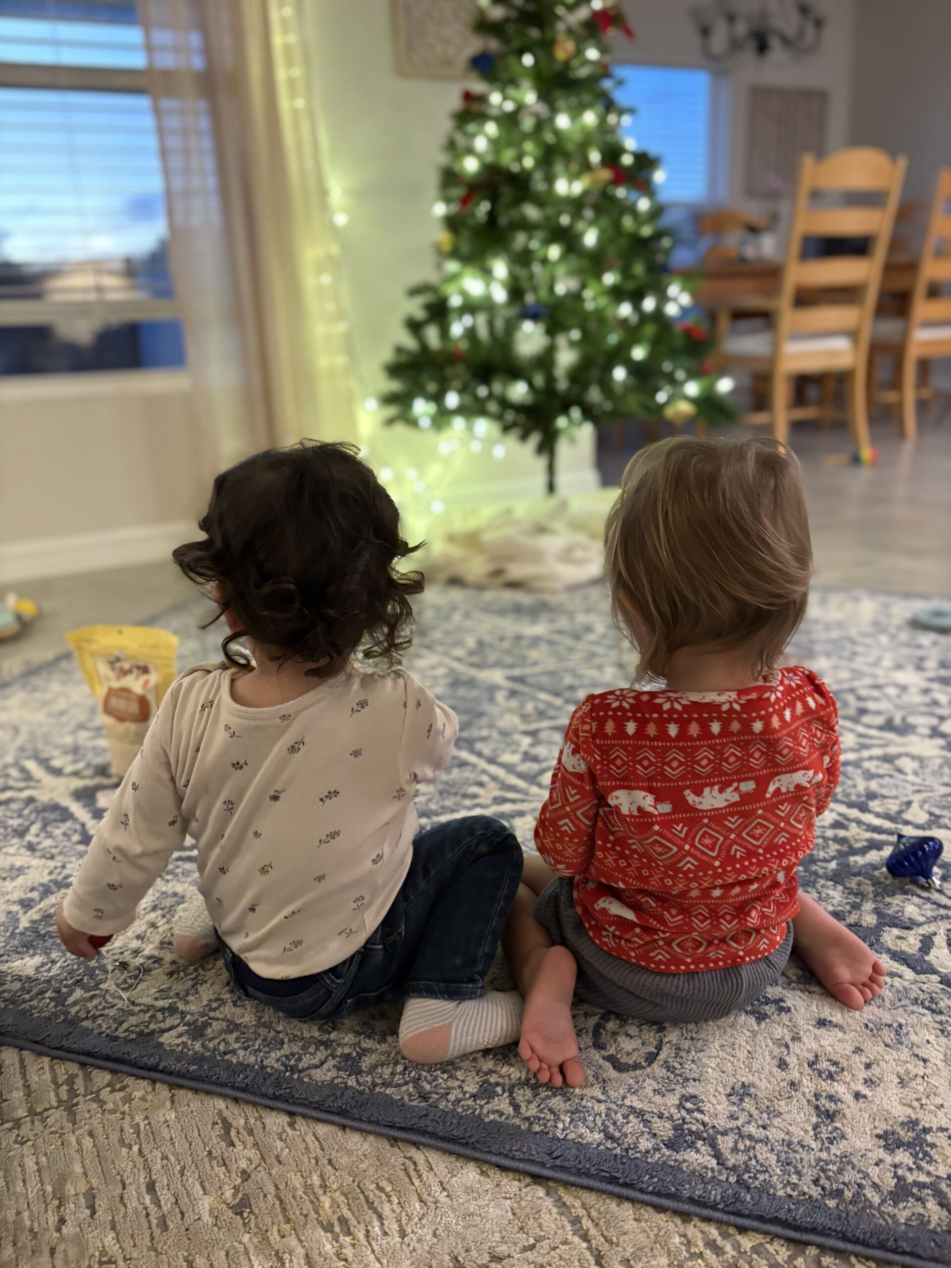 two young children sitting together in front of a christmas tree