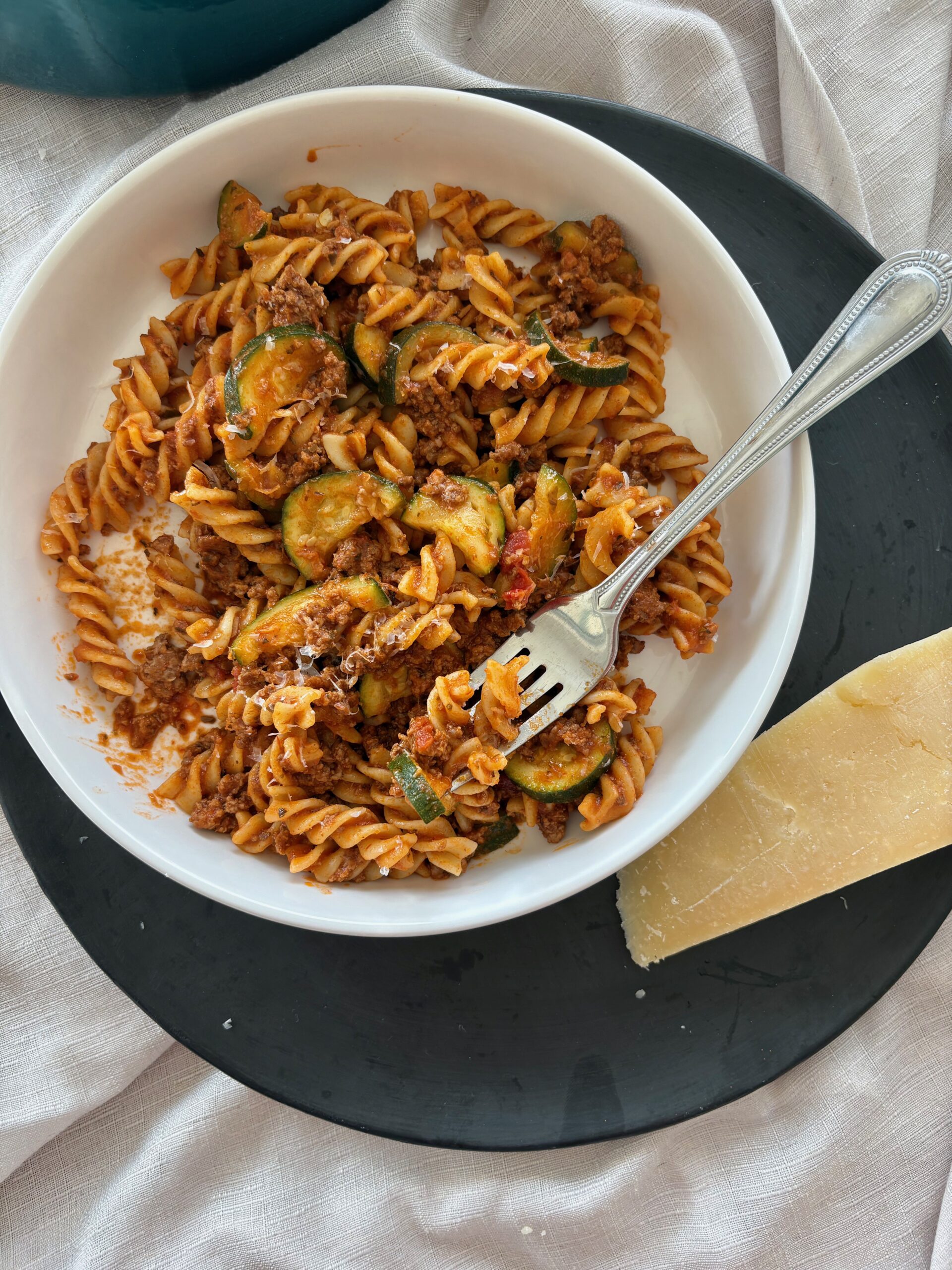 a white bowl of ground beef pasta with zucchini on a black plate